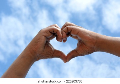 Two Black Hands Of An African American Man Held Together In A Heart Shape In Front Of Blue Sky Background.