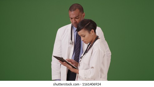 Two Black Medical Professionals Reviewing Data On Tablet Device On Green Screen