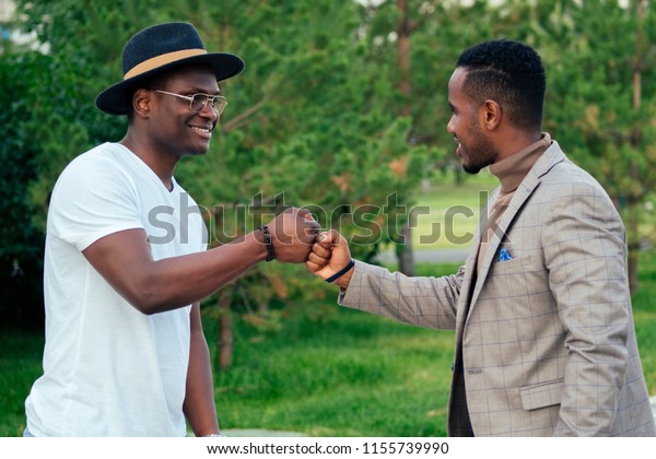 スタイリッシュなスーツを着た2人の黒人男性が夏の公園で会う アフリカ系アメリカ人の友人がヒスパニック系ビジネスマンを抱きしめ 互いに屋外でのチームワークに挨拶する 成功した取引のコンセプト の写真素材 今すぐ編集