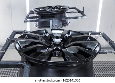 A Two black painted aluminum alloy wheel is mounted on a special frame during drying in a chamber in a vehicle body repair workshop. Auto service industry.