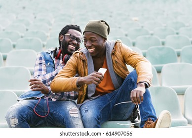Zwei schwarze Rennfreunde, die Spaß mit dem Handy haben. Konzept der Freunde