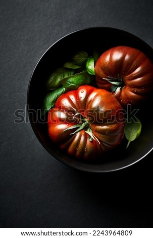 Two black tomatoes and basil leaves in a black dish. Close-up