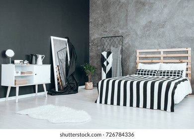 Two Black And White Jugs On Wooden Cupboard And Potted Plant In The Corner Of Room With Bed