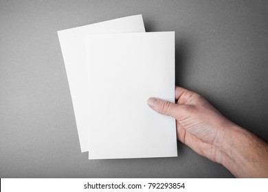 Two blank sheets of A5 for design, a mock-up in the hand of a European man.