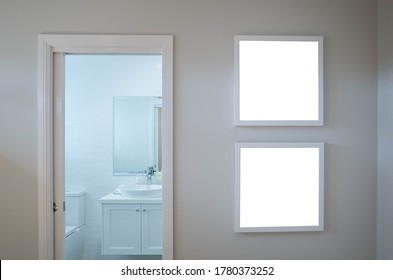 Two blank white square picture/artwork frame mockup template backgrounds on wall at the door of a bathroom/toilet.