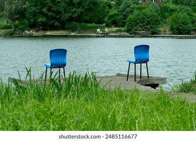 Two blue chairs sit on a wooden dock overlooking a lake. - Powered by Shutterstock