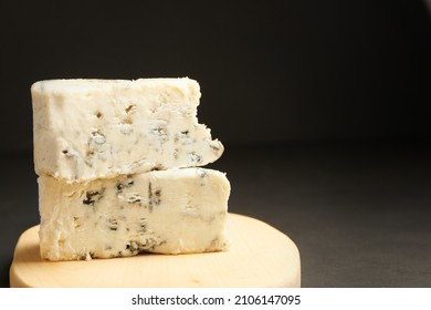 Two blue cheeses in stack on cutting board. Triangular piece of gorgonzola cheese on black background. - Shutterstock ID 2106147095