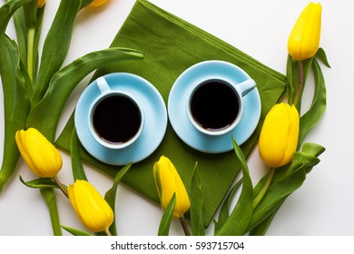 two blue cups of coffee on a table with green cloth and yellow tulips