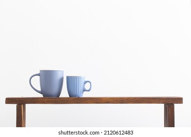 two blue cups on wooden shelf on white background