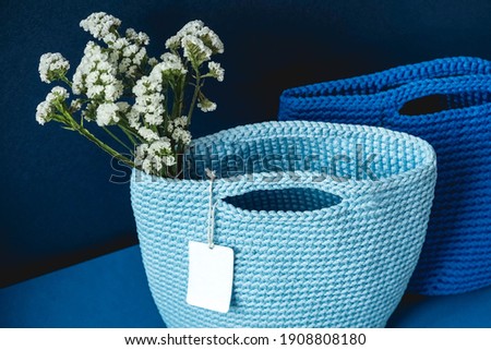 Two blue knitted handmade bag with flowers on a blue background. Copy, empty space for text.