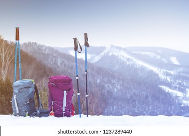 two blue and pink backpacks with walking sticks on the background of snow-capped mountains in the winter, the concept of romance and family walks in the hike