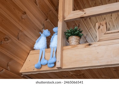 Two blue plush toys and a potted plant placed on a wooden shelf in a cozy, wooden interior setting, evoking warmth and comfort. - Powered by Shutterstock