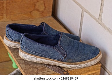 two blue shoes made of cotton fabric stand on a brown table board against a white brick wall
