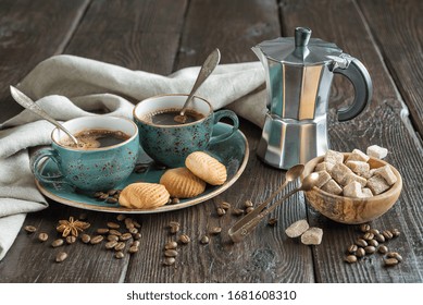 Two blue vintage cups of black coffee, cookies and geyser coffee maker surrounded by gray linen napkins, sugar pieces and coffee beans on old wooden table
