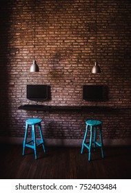 Two blue wooden stools next to desktop computers on the exposed brick interior wall of an internet cafe / co-working space
