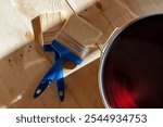 Two blue-handled paintbrushes on a light wooden floor next to a varnish can, illustrating wood floor treatment in a house