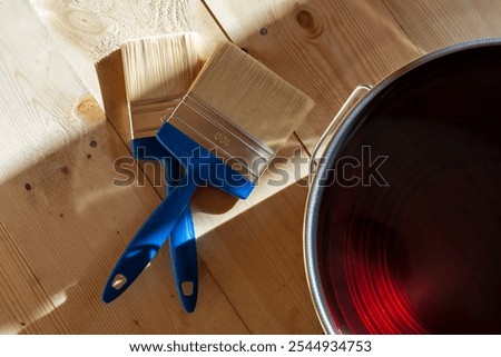 Two blue-handled paintbrushes on a light wooden floor next to a varnish can, illustrating wood floor treatment in a house