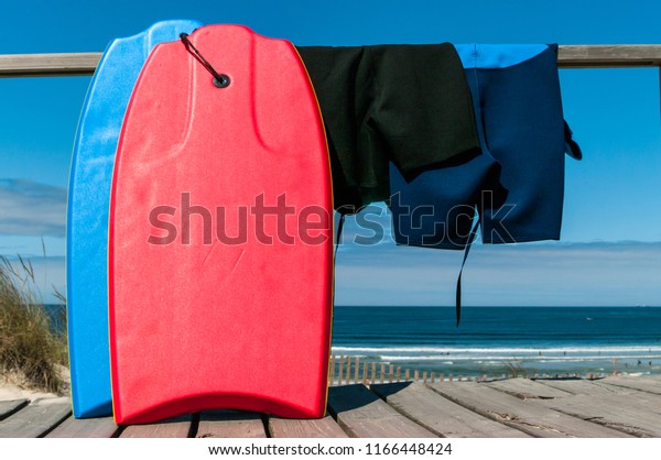 Two body boards and neoprene suits facing the beach\
and the ocean