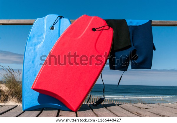 Two body boards and neoprene suits facing the beach\
and the ocean