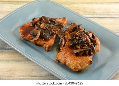 Two Boneless Pork Chops With Brown Mushroom Sauce On Blue Serving Plate