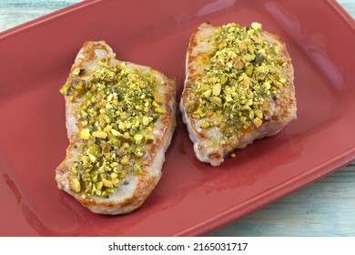 Two Boneless Pork Chops With Crushed Pistachios On Red Serving Plate