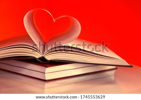 Two books, in the middle of opened book two pages glued of heart shape in the red background. Close up view.