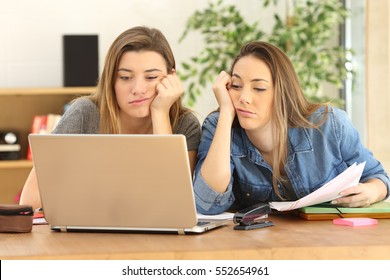 Two bored or tired students doing homework together on line with a laptop at home with a homey background