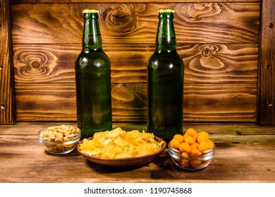 Two bottles of beer and different snacks on rustic wooden table