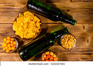 Two bottles of beer and different snacks on rustic wooden table. Top view
