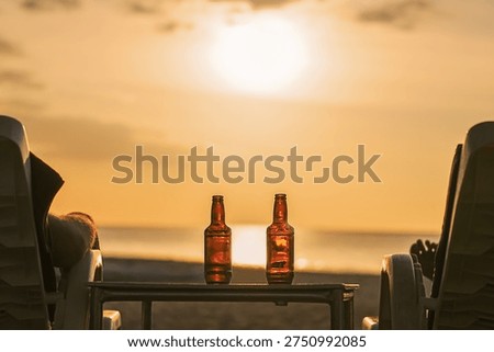 Two bottles of beer are on the table at sunset on the beach - Two friends or lovers are watching the sunset sitting in chairs back view. The concept travel and relaxing holidays with relaxing drinks. High quality photo