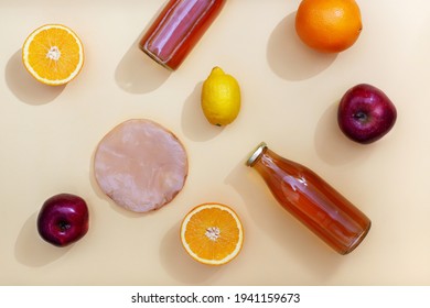 Two bottles of kombucha tea, scoby and fruits for additional flavors on yellow pastel background with shadows. Orange, lemon, apple. Healthy fermented drink. Flatlay mockup
