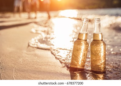 Two bottles of light beer on beach. Sea shore with waves. Group of friends on the background. - Powered by Shutterstock