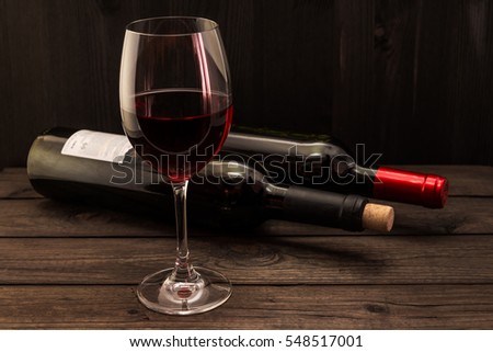 Two bottles of red wine with a glass on an old wooden table. Focus on the stem glass