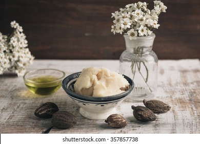 Two bowl of shea butter and oil with shea nuts on shabby wooden table.