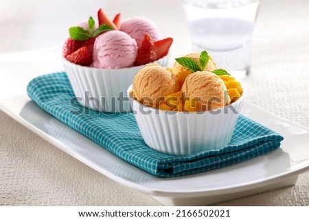 two bowls of ice cream with strawberry and mango flavors served with pieces of fruit according to their flavor