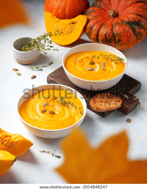 Two bowls of pumpkin\
cream soup with croutons and pumpkin seeds. Side view. Сomposition\
with autumn leaves
