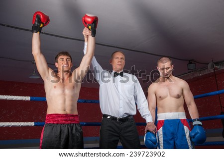 two boxer men standing in ring. referee lifting winner hand announcing victory