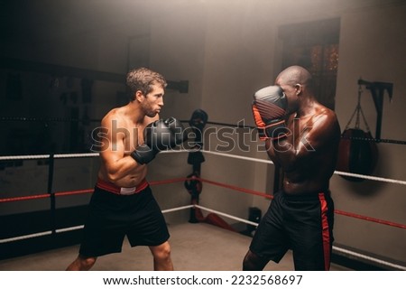 Two boxers standing in fighting position inside a boxing ring. Two athletic young men having a boxing match in a fitness gym.