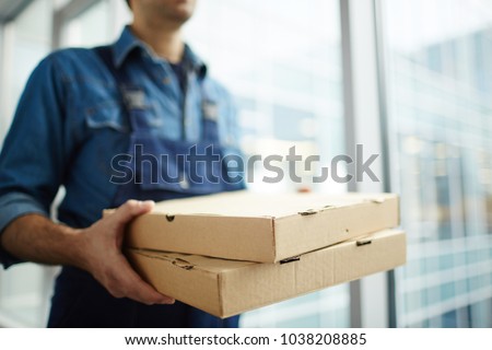 Two boxes with fast food being carried by delivery man in uniform for one of clients