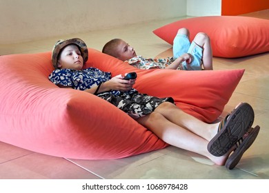 Two Boys (8-10 Years Old) Lie On The Floor Cushions And Watch TV. Side View