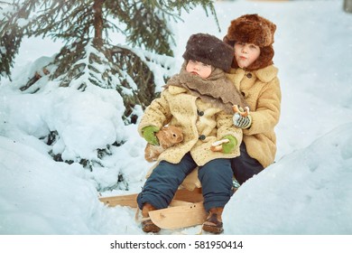 Two boys brother enjoy a sleigh ride. Child sledding. Toddler kid riding a sledge. Children play outdoors in snow. Kids sled in winter.  Little rabbits in the hands. 