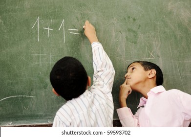 Two Boys In Classroom Thinking, Writing And Counting On Board