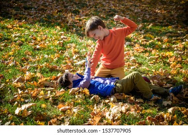 Two boys fighting outdoors. Friends wrestling in summer park. Siblings rivalry. Aggressive kid hold younger boy on ground, try to hit him.