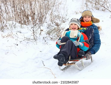 Two Boys Of A Friend Have Fun Sledding Down A Snow Slide.