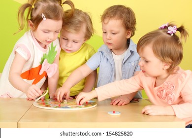 Two boys and two girls doing together wooden puzzle on the table