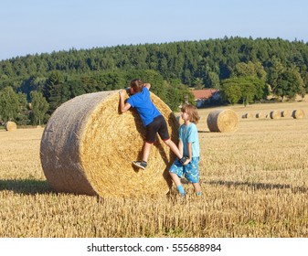 Two Boys Helping Each Other to Climb a Bale of Hay