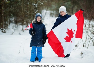 Two Boys Holding Flag Of Canada On Winter Landscape.