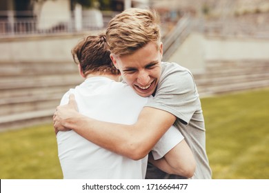 Two boys hugging each other in college campus. High school students smiling and giving each other a hug outdoors.