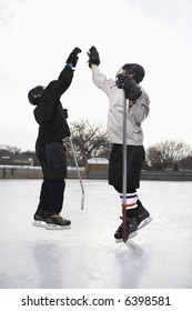 Two Boys In Ice Hockey Uniforms Giving Eachother High Five On Ice Rink.