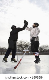 Two Boys In Ice Hockey Uniforms Giving Eachother High Five On Ice Rink.